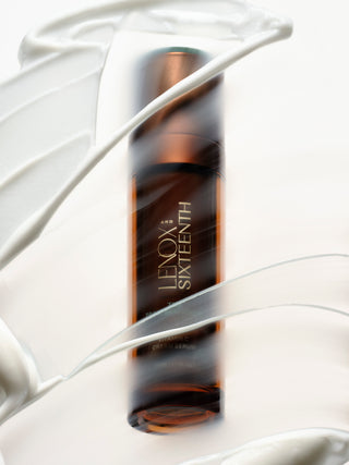 Bottle standing amidst swirling cream texture, white background.