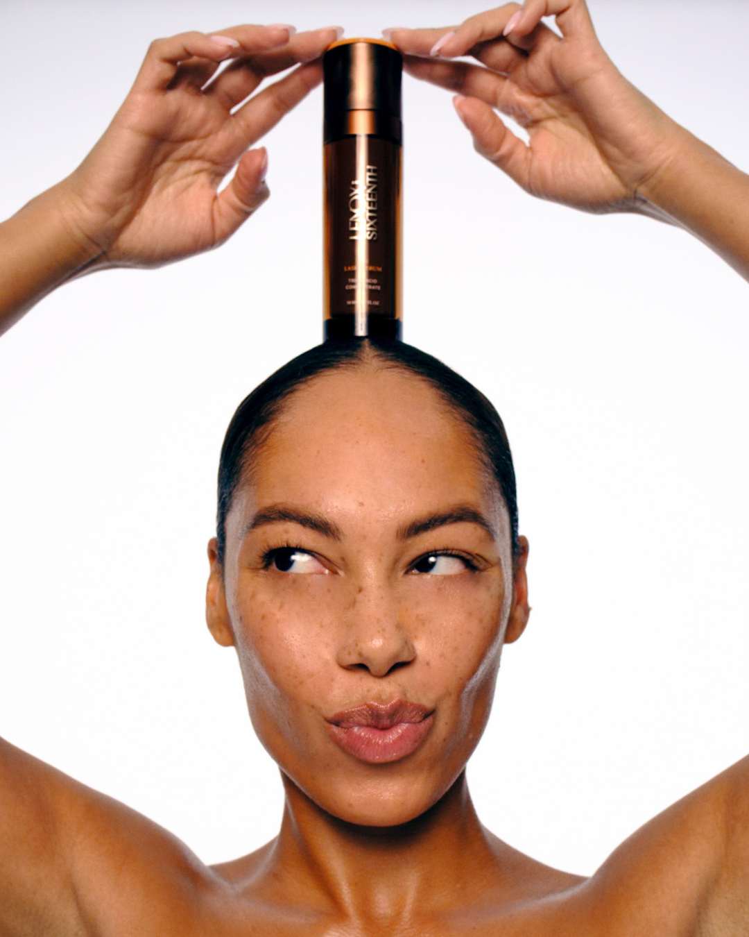 Bottle balanced on woman's head, hands steadying, white background.