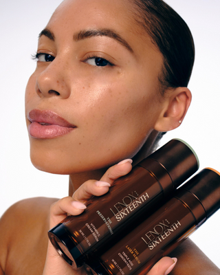 Person holding skincare bottles against their face, neutral background.
